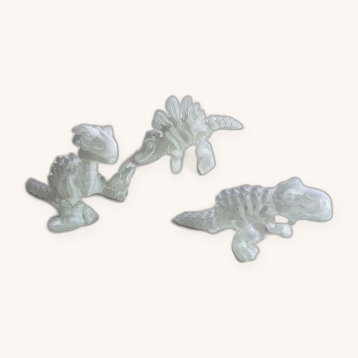 Os três Dinos Brilha no Escuro (T-Rex, Velociraptor e Espinossauro) lado a lado, na cor branco-perolada de dia